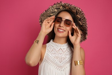 Beautiful young woman with straw hat and sunglasses on crimson background. Stylish headdress