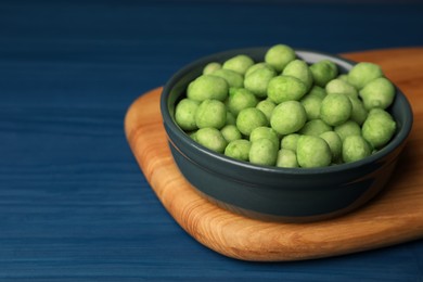 Tasty wasabi coated peanuts in bowl on blue wooden table, closeup. Space for text