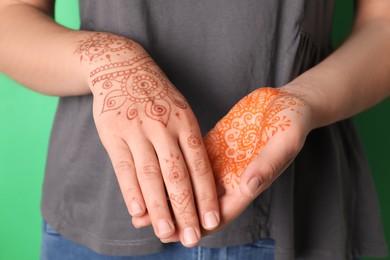 Woman with henna tattoos on hands against green background, closeup. Traditional mehndi ornament