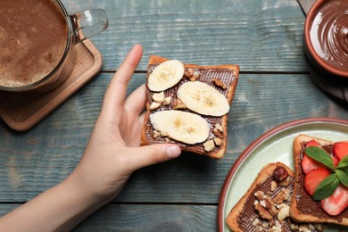 Woman holding tasty toast with chocolate spread, nuts and banana at wooden table, top view