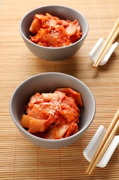 Photo of Bowls of spicy cabbage kimchi and chopsticks on bamboo mat