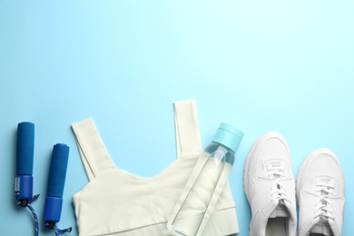Sportswear, jump rope and water bottle on light blue background, flat lay with space for text. Gym workout