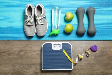Flat lay composition with scales, apples and sport equipment on wooden background. Weight loss