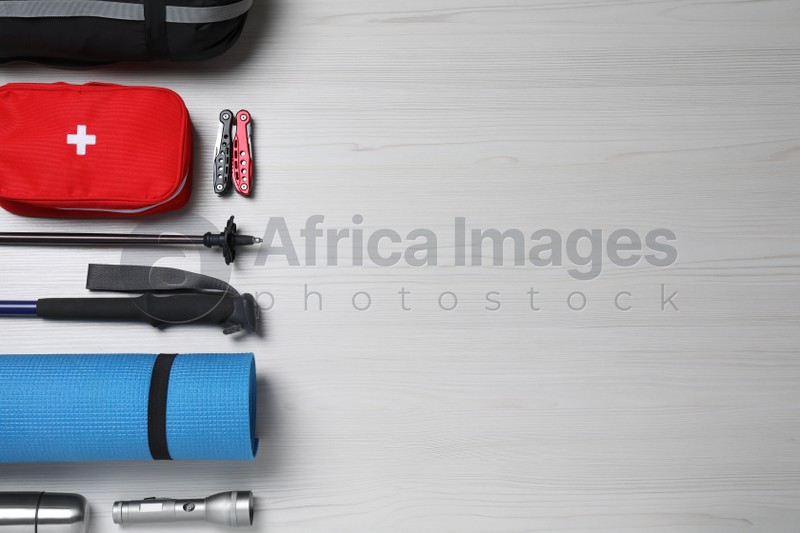 Flat lay composition with trekking poles and other hiking equipment on white wooden background, space for text