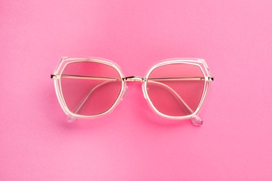 New stylish sunglasses on pink background, top view