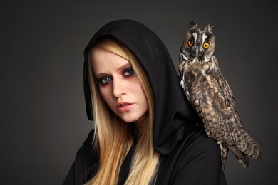 Witch in black mantle with owl on dark background. Scary fantasy character