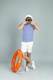 Photo of Sailor with binoculars and ring buoy on light grey background
