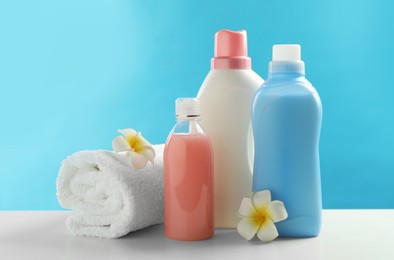 Bottles of laundry detergents, towel and plumeria flowers on white table