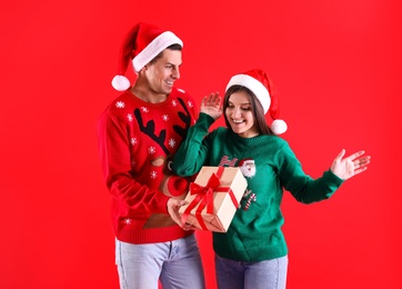 Man presenting Christmas gift to his girlfriend on red background