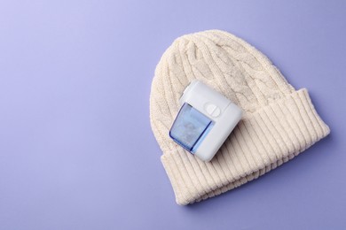 Photo of Fabric shaver with knitted hat on lilac background, top view. Space for text