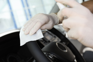 Man cleaning steering wheel with wet wipe and antibacterial spray in car, closeup