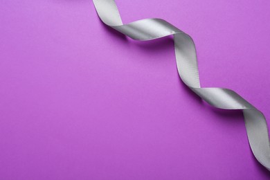 Beautiful silver ribbon on purple background, top view. Space for text