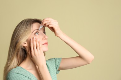 Young woman using eye drops on pale olive background