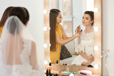 Makeup artist preparing bride before her wedding in room