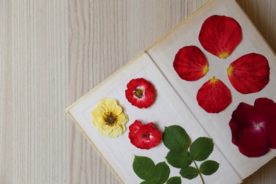 Book with beautiful flowers, leaves and petals prepared for drying on wooden table, top view