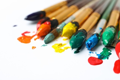 Brushes with colorful paints on white background, closeup