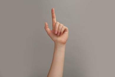 Woman showing index finger on grey background, closeup