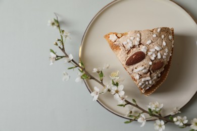 Photo of Plate with piece of delicious Italian Easter dove cake (traditional Colomba di Pasqua) and flowering branches on light grey table, top view. Space for text