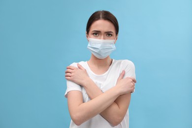Woman in mask suffering from fever on light blue background. Cold symptoms