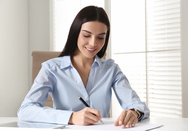 Young businesswoman writing at table in office