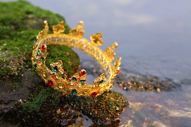 Beautiful golden crown on stone with green moss near river outdoors, closeup. Fantasy item