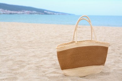 Stylish straw bag on sand near sea, space for text. Beach accessory