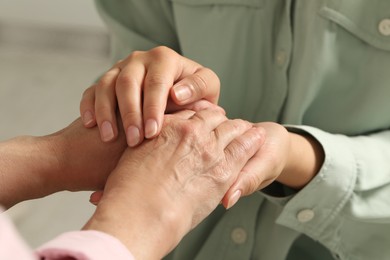 Young and elderly women holding hands indoors, closeup