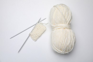 Soft woolen yarn, knitting and metal needles on white background, top view