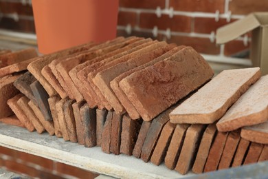 Many decorative bricks on scaffolding near wall, closeup. Tiles installation process