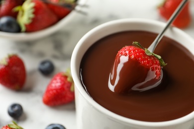 Dipping strawberry into fondue pot with chocolate, closeup