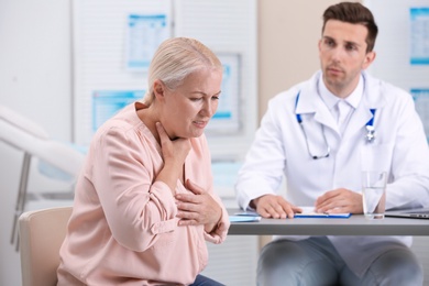 Coughing mature woman visiting doctor at clinic