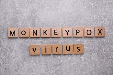 Photo of Words Monkeypox Virus made of wooden squares with letters on light grey background, top view
