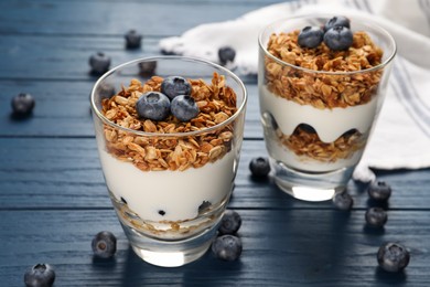 Glasses of tasty yogurt with muesli and blueberries on blue wooden table