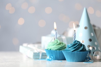 Photo of Delicious birthday cupcakes with cream and burning candles on white table. Space for text