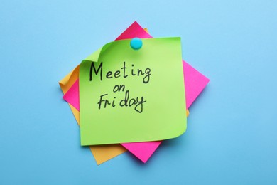 Paper note with words Meeting on Friday pinned to light blue background