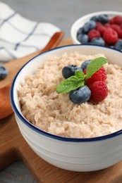 Tasty oatmeal porridge with berries on grey wooden table, closeup