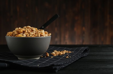 Ceramic bowl with granola on black wooden table, space for text. Cooking utensil