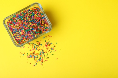 Colorful sprinkles in bowl on yellow background, top view with space for text. Confectionery decor