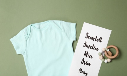 Photo of Bodysuit, list of baby names and toy on green background, flat lay