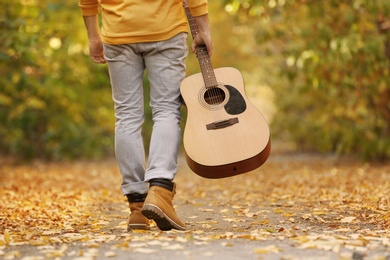 Young man with guitar walking in autumn park, closeup