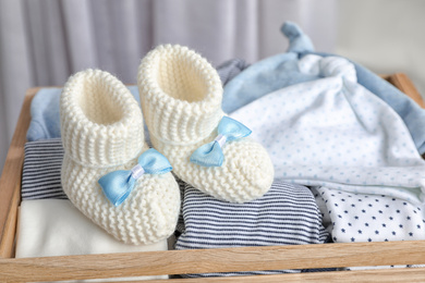 Pair of knitted booties and child's clothes in wooden crate, closeup