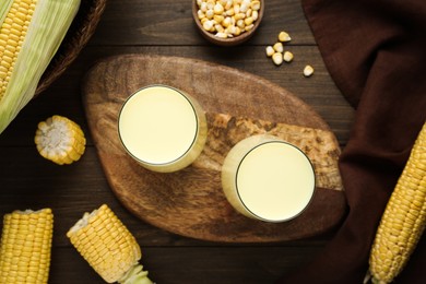 Tasty fresh corn milk in glasses and cobs on wooden table, flat lay
