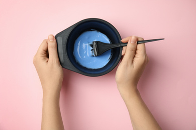 Woman preparing dye for hair coloring on pink background, top view