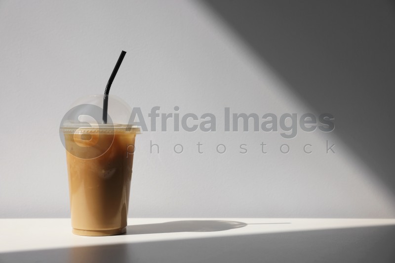 Photo of Plastic takeaway cup of delicious iced coffee on white table under sunlight, space for text