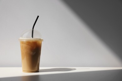 Plastic takeaway cup of delicious iced coffee on white table under sunlight, space for text