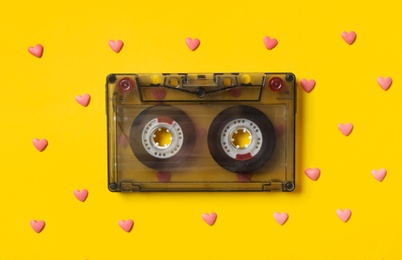 Music cassette and pink heart shaped sprinkles on yellow background, flat lay. Listening love songs