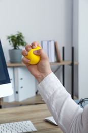 Man squeezing yellow stress ball in office, closeup