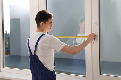 Worker measuring plastic window indoors. Installation process