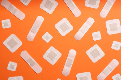 Different types of sticking plasters on orange background, flat lay
