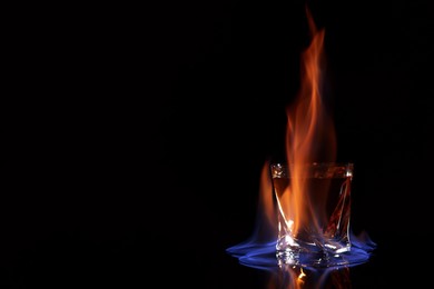 Glass with flaming vodka on black background, space for text